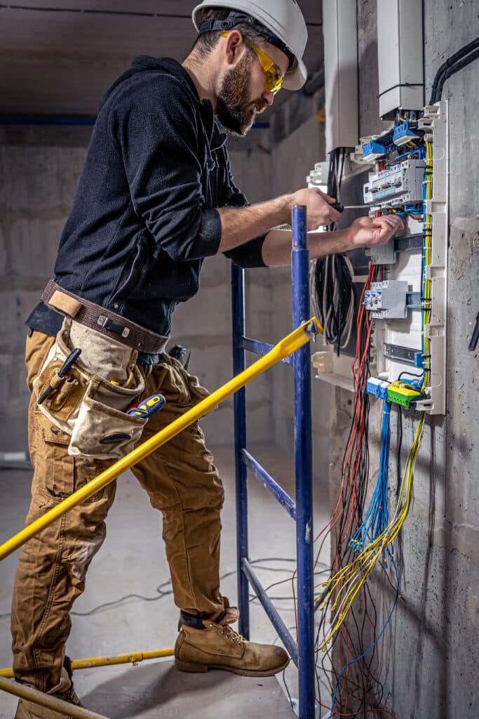 A male electrician works in a switchboard with an electrical connecting cable after getting ISN certified for his hiring client.