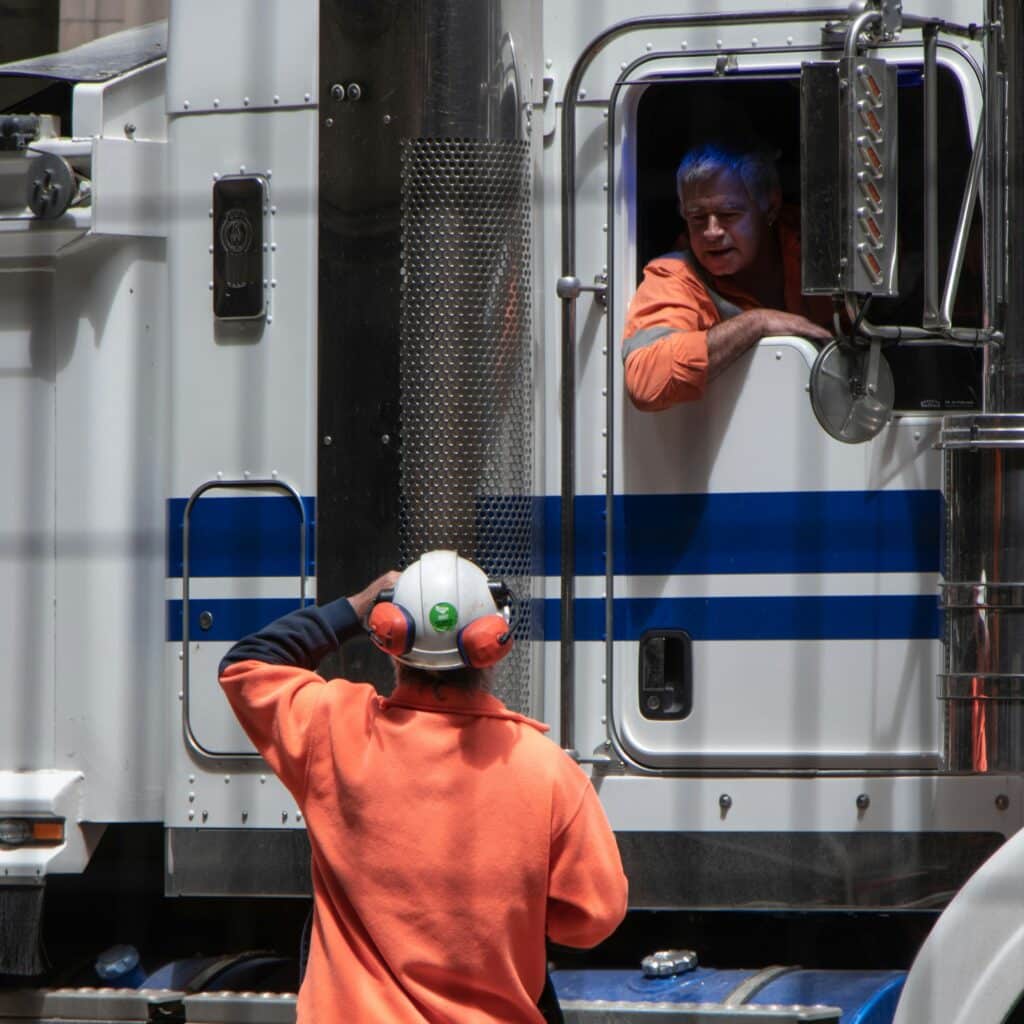 Two trucking fleet drivers talking to each other as they go through their daily safety checklist. One drive is in the truck talking out the window to the other.